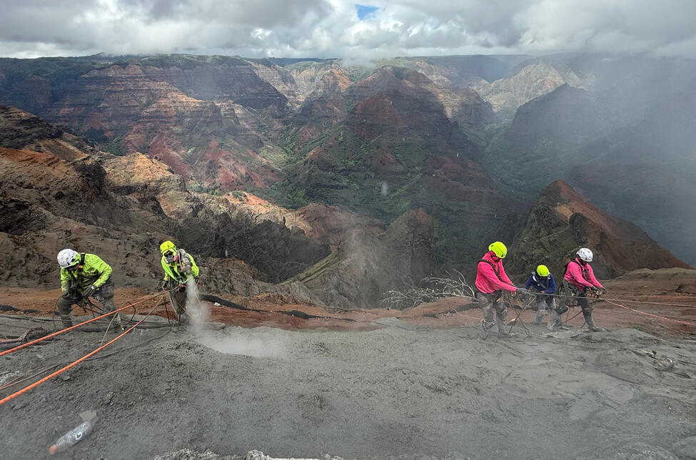 Crew applying shotcrete with Waimea Canyon visible behind them