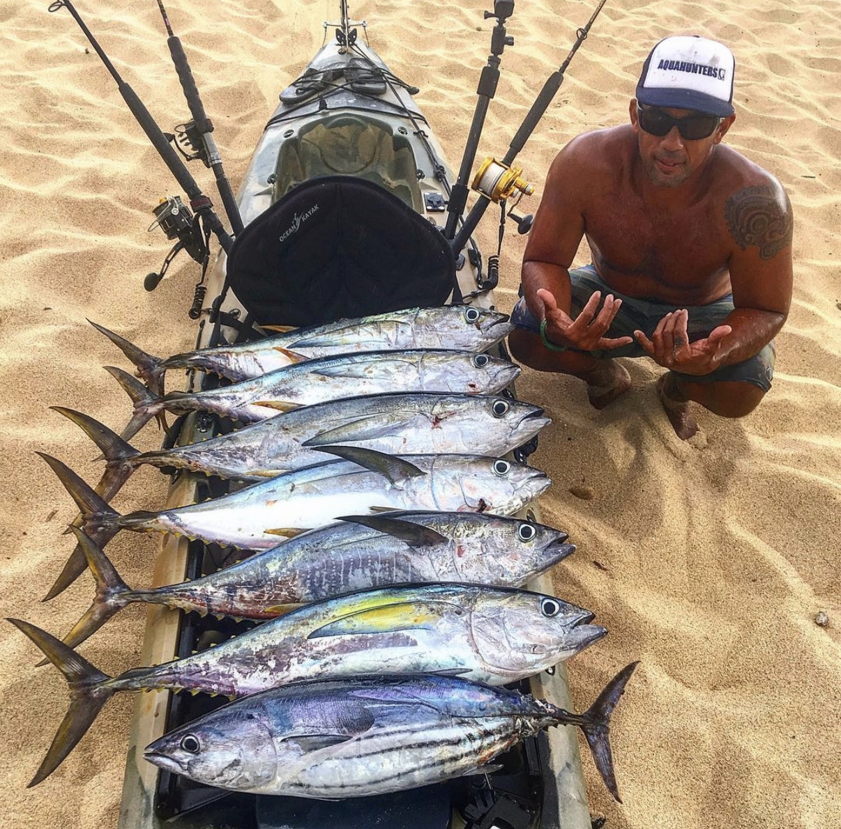 Isaac on the beach beside his kayak and a row of freshly caught fish